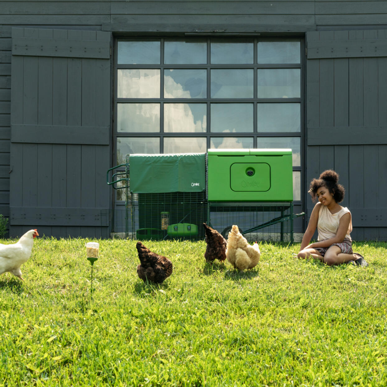 Woman sitting on the grass next to her chicken coop watching her chickens roam