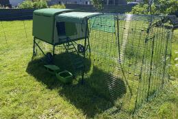Een groen kippenhok met een ren in een tuin