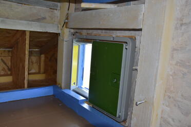 An Omlet automatic door opener attached on the inside of a wooden coop.