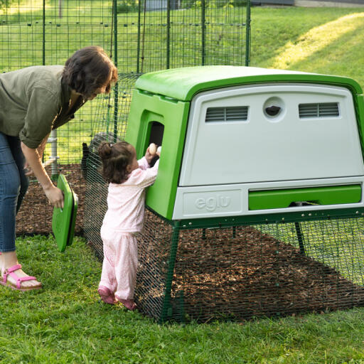 Eine mutter mit ihrer tochter, die in einen modernen hühnerstall greift, um eier zu sammeln