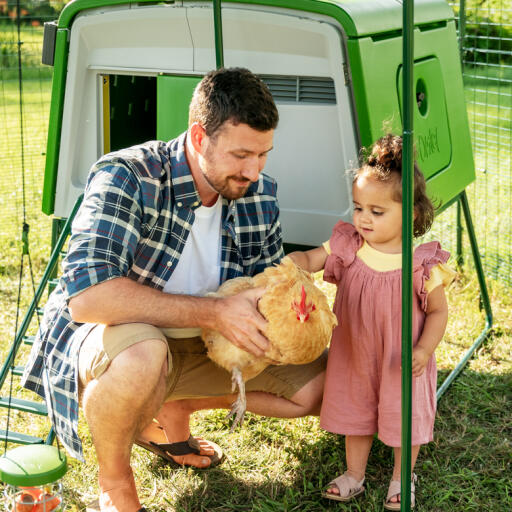 Mann mit seiner tochter, die ein huhn in einem hühnerstall hält.