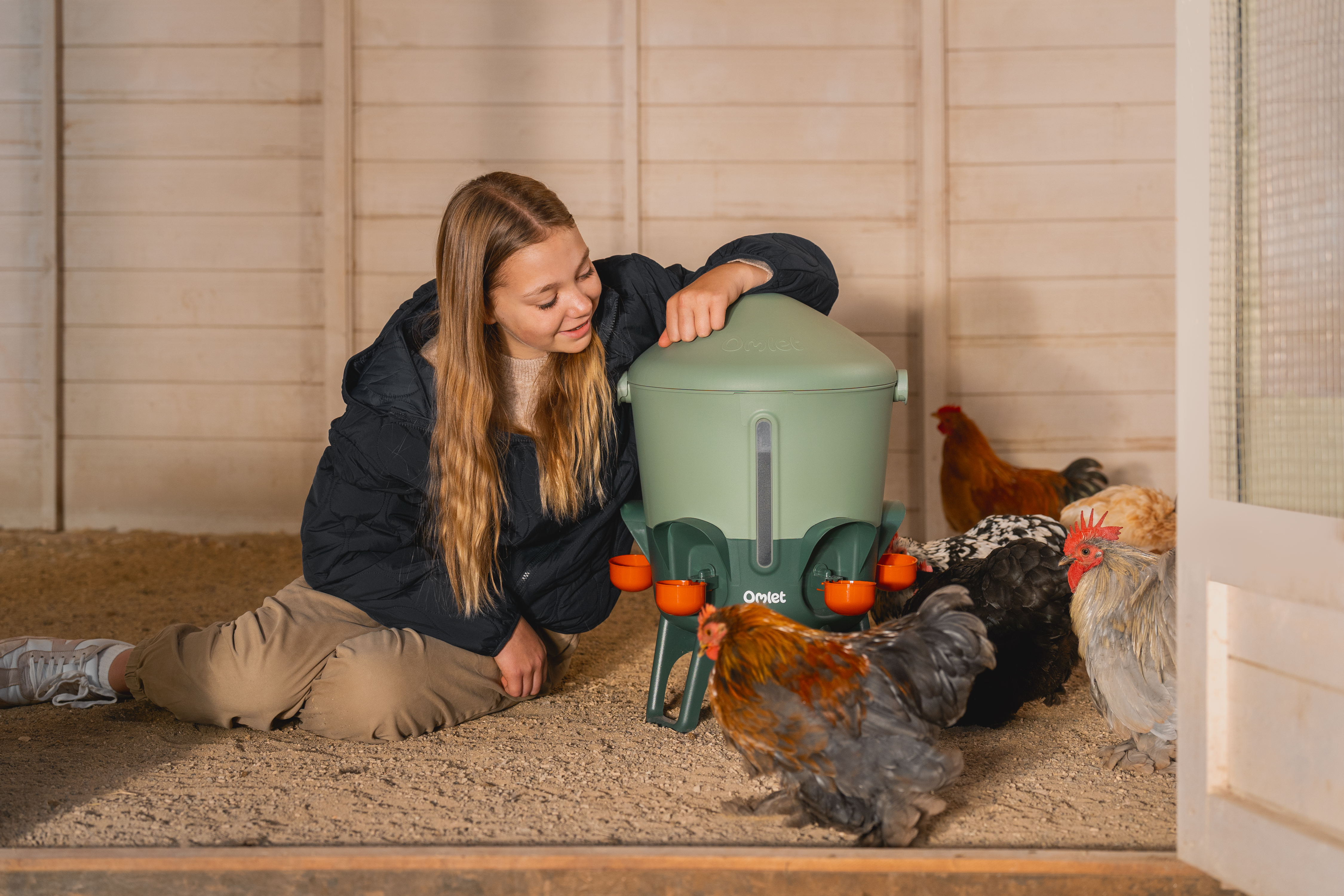 girl sitting next to chickens drinking from omlet insulated drinker