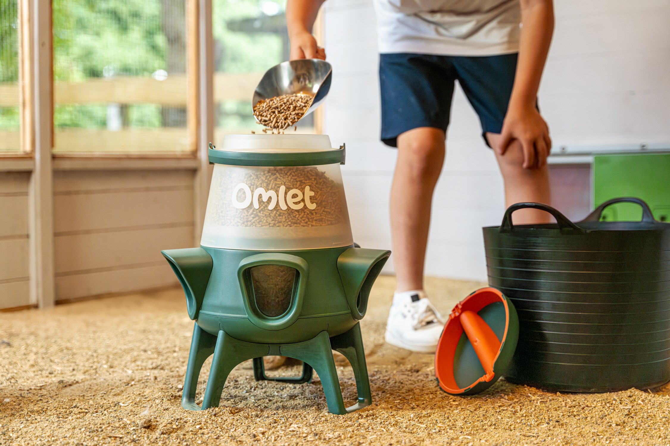 boy refilling no waste chicken feeder in a wooden chicken coop